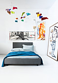 Grey bed in corner of room decorated with modern artworks
