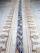 Strip of modern, multicoloured, geometric tiles on antique mosaic floor