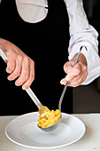 Professional chef arranging cooked fettucine pasta on a white plate