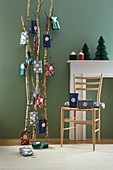 Gift bags hung from birch branches as Advent calendar against green wall