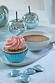 Cupcake and cup of coffee on table set in pale blue and pink