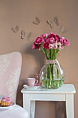 Vase of ranunculus below butterfly decorations on brown wall