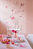 Romantically set table in front of pink wall decorated with butterflies