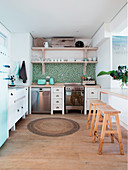 Blue-and-green mosaic-tiled splashback and white kitchen cabinets in light-flooded kitchen