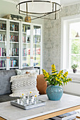 Blue vase of yellow loosestrife and glass-fronted bookcases in living room