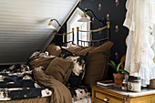 Black and brown bed linen on metal bed below sloping ceiling