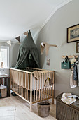 Cot with green canopy in room with pale grey walls