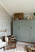 Antique grey cabinet in child's bedroom with patterned wallpaper