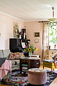 Verschiedene Sitzmöbel um runden Tisch, im Hintergrund Klavier im Wohnzimmer mit rosa Wänden