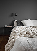 Chunky knitted blanket on double bed against grey bedroom wall