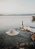 Hat, bottle of Champagne, glasses and lemons on rock next to sea