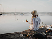 Frau sitzt mit Sektglas am Steinufer eines Sees
