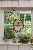 Kranz und Pflanzen am Fenster mit Blick in den sommerlichen Garten