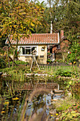 Gelbes Gartenhaus im spätsommerlichen Garten mit Teich