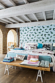 Double bed and bedroom bench in front of pale blue partition wall with pattern of birds