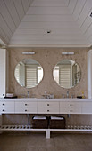 Twin sinks with white base units below round mirrors in beach house