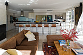 Wohnraum mit brauner Polstergarnitur im Sitzbereich und offener Küche mit Frühstückstheke