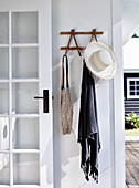 Garderobe mit Sonnenhut, Tuch und Tasche an weißer Wand, neben Sprossentür