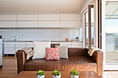 Cognac leather couch in front of white kitchen counter in open-plan interior