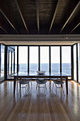 Dining table and metal chairs in front of glass wall with sea view