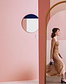 Round mirror on pink wall, reflection of woman in oval mirror