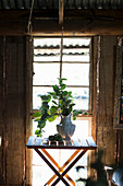 Vase auf kleinem Klapptisch vor Fenster in rustikaler Holzhütte