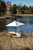 Picnic on rustic wooden table below parasol on lake shore