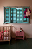 Vintage-Kinderzimmer in Rosa mit Gitterbett unter Fenster mit blauen Fensterläden