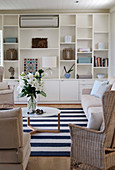 White fitted shelving in seating area with pale rattan and upholstered furniture