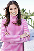 A young brunette woman wearing a pink roll-neck jumper