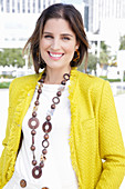 A young woman wearing a chunky necklace, a white jumper and a yellow bouclé jacket