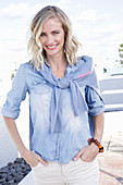 A blonde woman wearing a denim shirt with a jumper over her shoulders