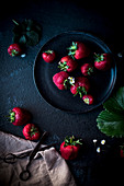 Stillleben mit Erdbeeren und Gänseblümchen auf dunklem Untergrund