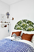 Bed with blue-and-white striped bed linen and exotic leaf pattern on headboard