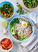 Asian noodle soup with kimchi, edamame, pork, egg, coriander, leek and pak choi
