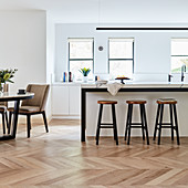 Barstools at counter and dining table in open-plan kitchen with parquet floor