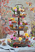 Kleine Sträuße aus Rosen und Hagebutten mit Herbstlaub auf Metall-Etagere als Tischdekoration