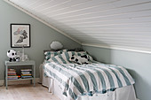 Bed with striped bed linen in child's bedroom with sloping ceiling
