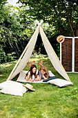 Two girls playing in tent behind floor cushions in garden