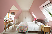 Double bed and desk in attic bedroom with pink walls