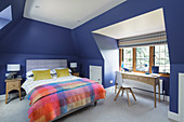 Double bed and desk in attic bedroom with blue walls