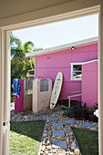 Blick auf pinkes Haus mit Außendusche und Surfbrett im Garten
