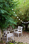 Zwei Holzstühle und Lichterkette im Garten