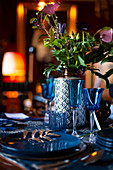 Blaue Gläser und Teller auf festlich gedecktem Tisch mit Blumen