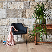 Black upholstered chair, console table and plant against stone wall