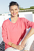 A young woman with long hair wearing a pink jumper and white trousers