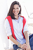 A brunette woman wearing a light shirt with a red jumper over her shoulders