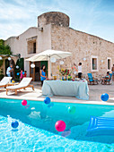 Partybuffet mit Sonnenschirm an sonnigem Pool mit bunten Luftballons