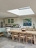 Dining table positioned below skylight and country-house kitchen in open-plan interior