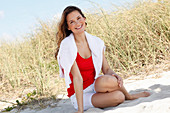 A woman with long hair wearing a red top with a jumper over her shoulders and white shorts